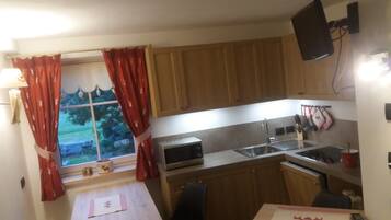 A compact kitchen with wooden cabinets, a microwave, a sink, and a window with red curtains.