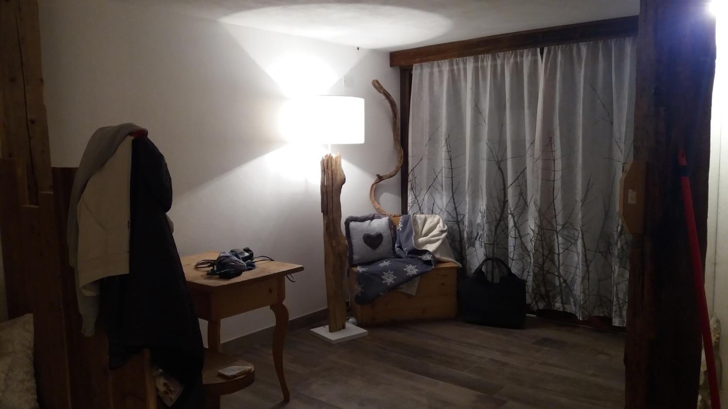 Een kamer met een houten vloer, een bureau met lamp, een stoel en een raam met gordijnen.