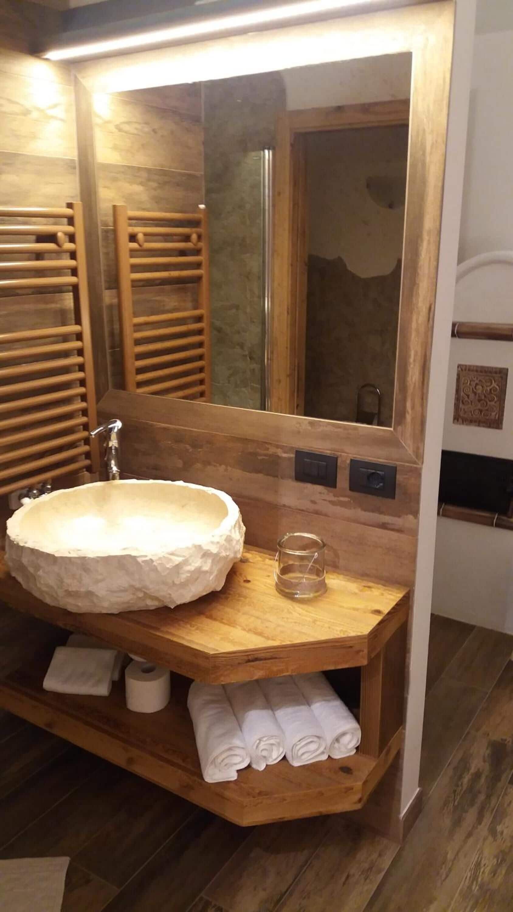 Ein Badezimmer mit einem großen, weißen, steinartigen Waschbecken, Holzregalen, einem Spiegel und einem Handtuchhalter.