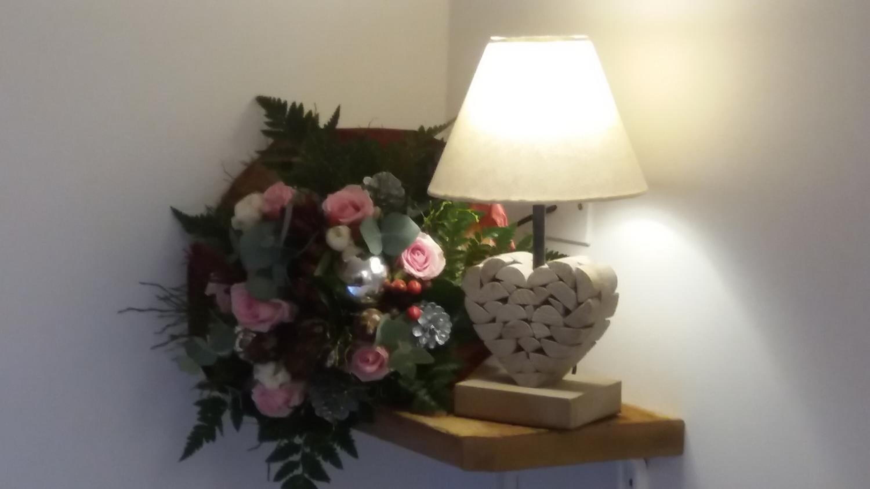 Una lámpara de pared con pantalla blanca y una decoración de flores y follaje.