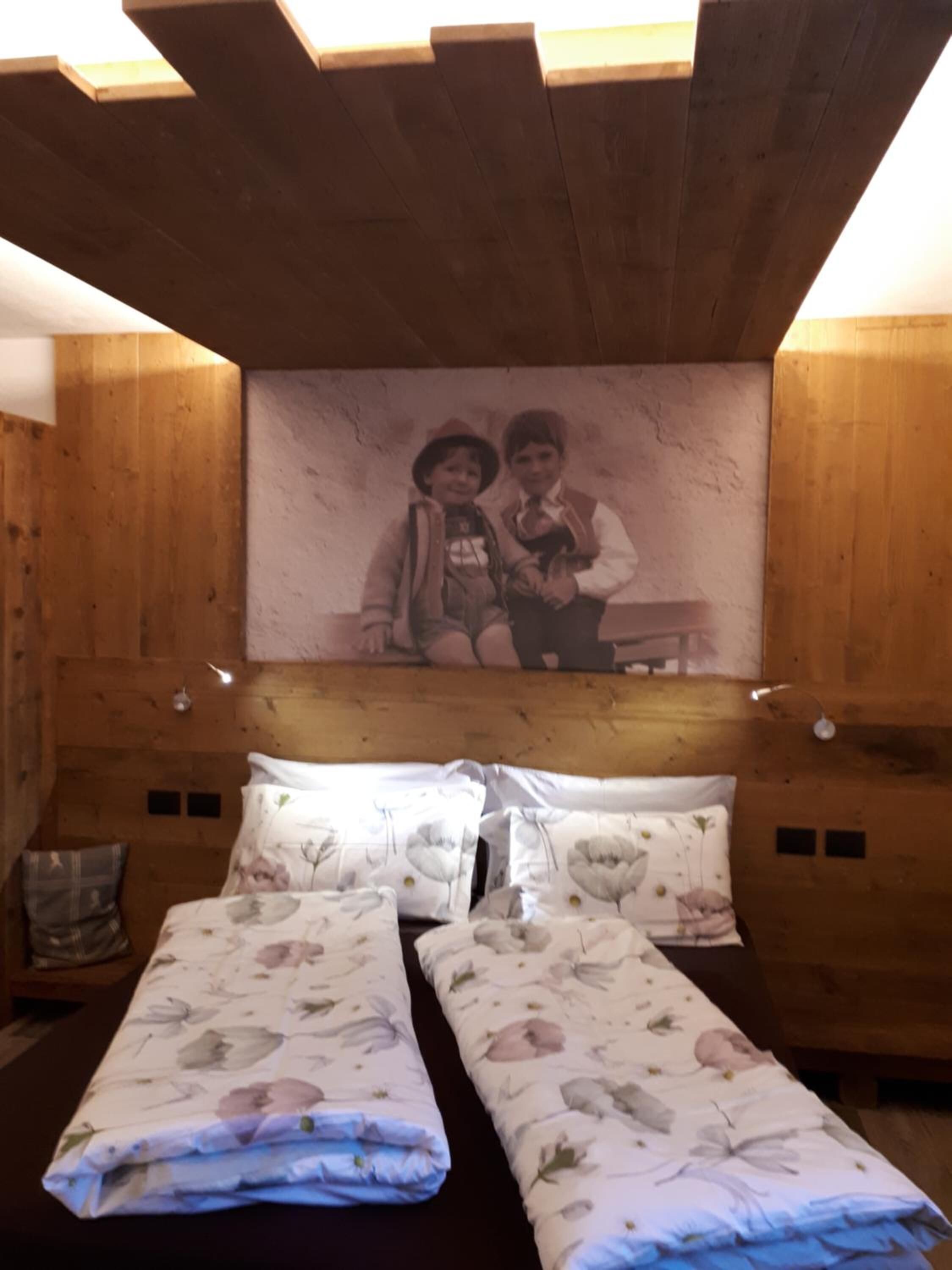 A wooden cabin room with a bed, two pillows, a wall-mounted picture, and a small table.