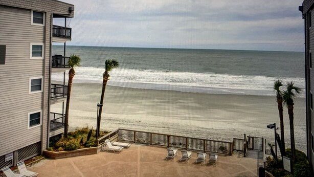 A beachfront view from an apartment balcony with a sandy beach, ocean waves, and palm trees. - Beachfront/Pool Murrells/GardenCity/Surfside 
Wkly/MilitaryFirePoliceNurse Discs (Murrells Inlet)