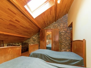 Un dormitorio con techo de madera y paredes de piedra, tragaluz y cama con cubierta azul.