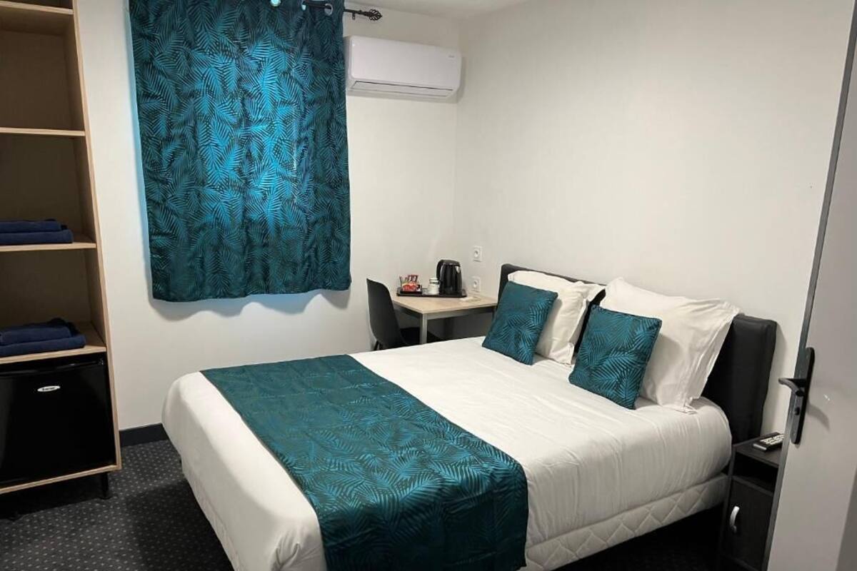 A hotel room with a bed, a desk, a chair, and a wardrobe.