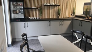 A modern kitchen with a built-in refrigerator, wooden panel wall, and a dining area with a table and chairs. - Hotel de la Paix Lyon Sud Givors (Givors)