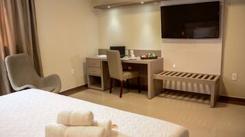 A hotel room with a bed, a desk with a computer, a chair, and a TV.