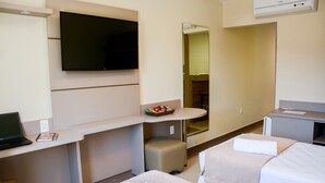 A hotel room with a flat-screen TV, a desk with a laptop, a small seating area, a bed with a white comforter, and a mirror. - Paracambi Top Hotel (Paracambi)