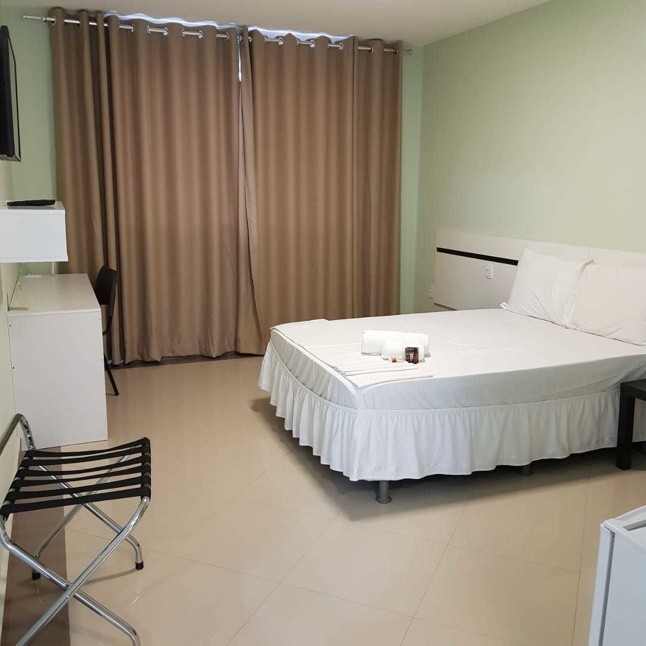 A hotel room with a bed, a desk, a chair, and a curtain.