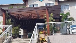 A building with a staircase leading to a covered entrance, a blue star logo, and a parked car in the background. - Paracambi Top Hotel (Paracambi)
