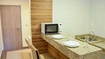 A compact kitchen with a microwave, two white plates, a wine glass, and a sink.