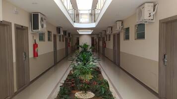Un pasillo de hotel con una jardinera central, extintor y unidades de aire acondicionado en las paredes.