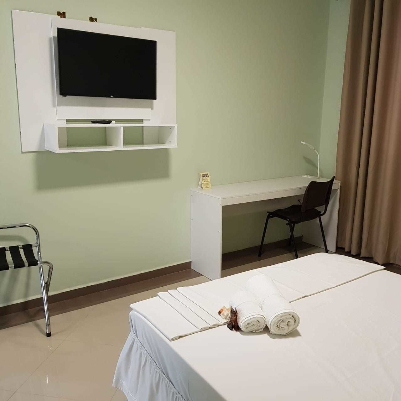 A hotel room with a bed, a desk, a chair, a television, and a sign indicating no smoking.