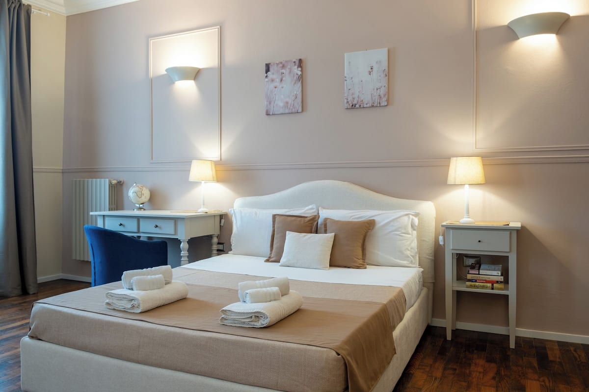 Una habitación de hotel con una cama grande, dos mesitas de noche, un escritorio y una silla.