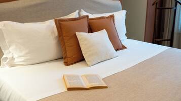 Cama bem arrumada com almofadas brancas e castanhas, um livro aberto na cama e um cabide de madeira na parede.
