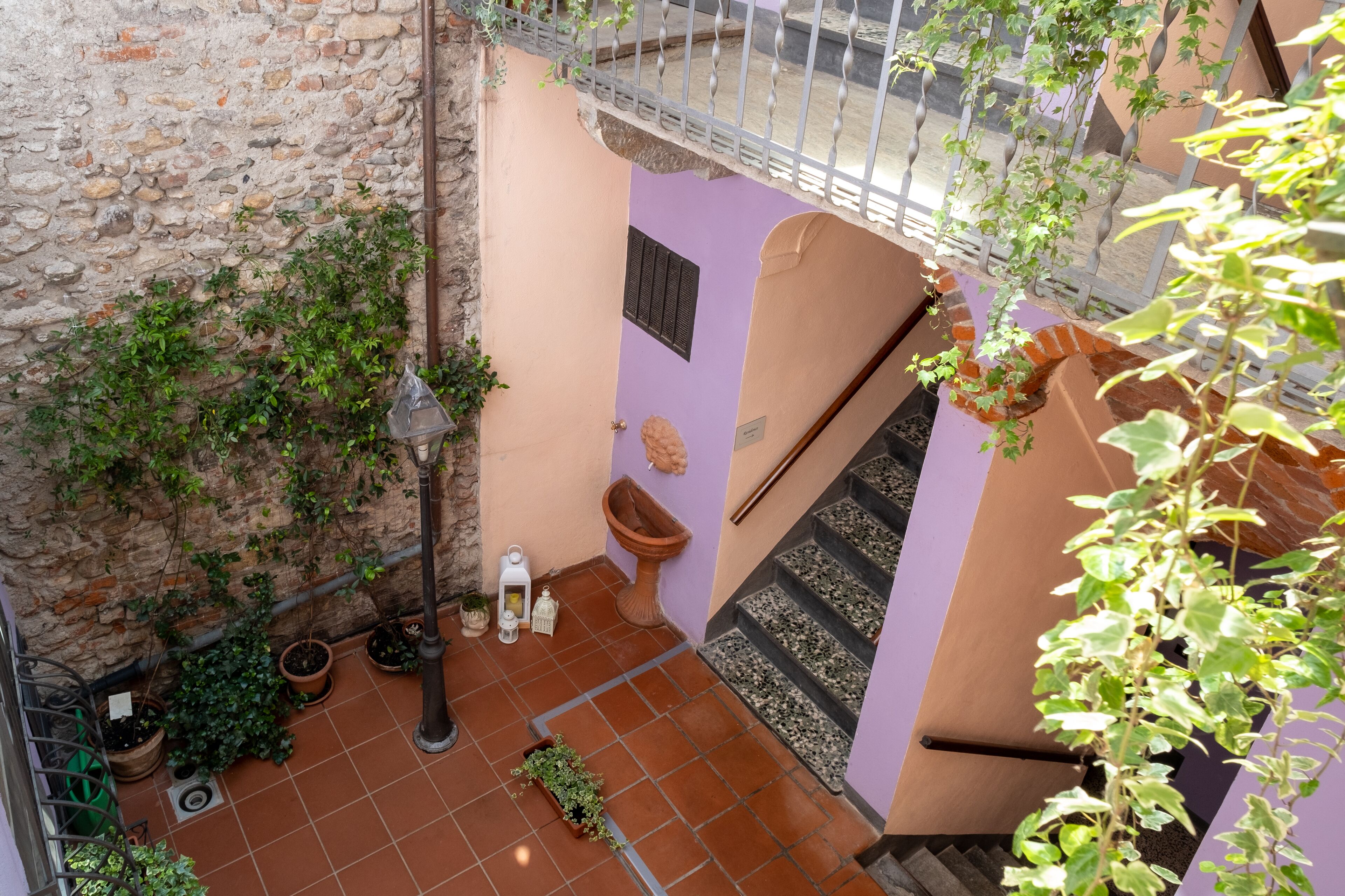 Une cour intérieure avec un mur en pierre, des carreaux de terre cuite, un escalier en bois et des plantes en pot.