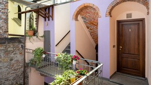 A narrow alleyway with a wooden door marked '3', a brick archway, and a metal railing with potted plants. - Residence Ferraud (Pinerolo)