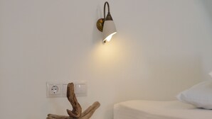 A white bedside table with a wooden sculpture and a wall-mounted light fixture. - Nufaro Traditional Studios (Naxos)