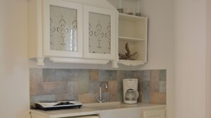 A compact kitchen with white cabinetry, a built-in coffee maker, and a small refrigerator. - Nufaro Traditional Studios (Naxos)