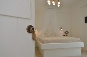 A bedroom with a bed, a bedside table, a nightstand, a wall-mounted light, and a door with a keyring. - Nufaro Traditional Studios (Naxos)