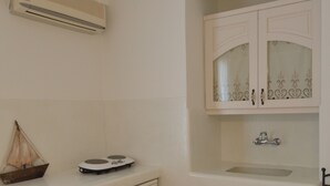 A compact kitchen with a built-in dishwasher, a small sink, and a decorative cabinet with glass doors. - Nufaro Traditional Studios (Naxos)