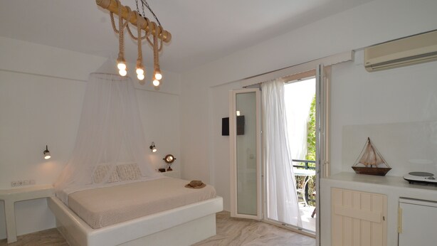 A bedroom with a bed, bedside tables, a ceiling light fixture, and a sliding glass door leading to an outdoor area. - Nufaro Traditional Studios (Naxos)