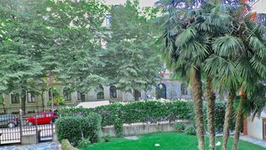 A courtyard with a stone pathway, green lawn, palm trees, and a red car parked near a gate. - Aiello Suites Executive (Milan)