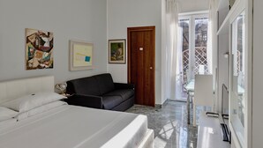 A modern hotel room with a bed, a sofa, a desk with a computer, and artwork on the walls. - Aiello Suites Executive (Milan)