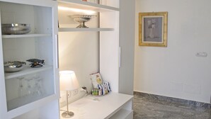 A well-lit room with a white console table, a lamp, a framed picture on the wall, and a shelf with decorative items. - Aiello Suites Executive (Milan)