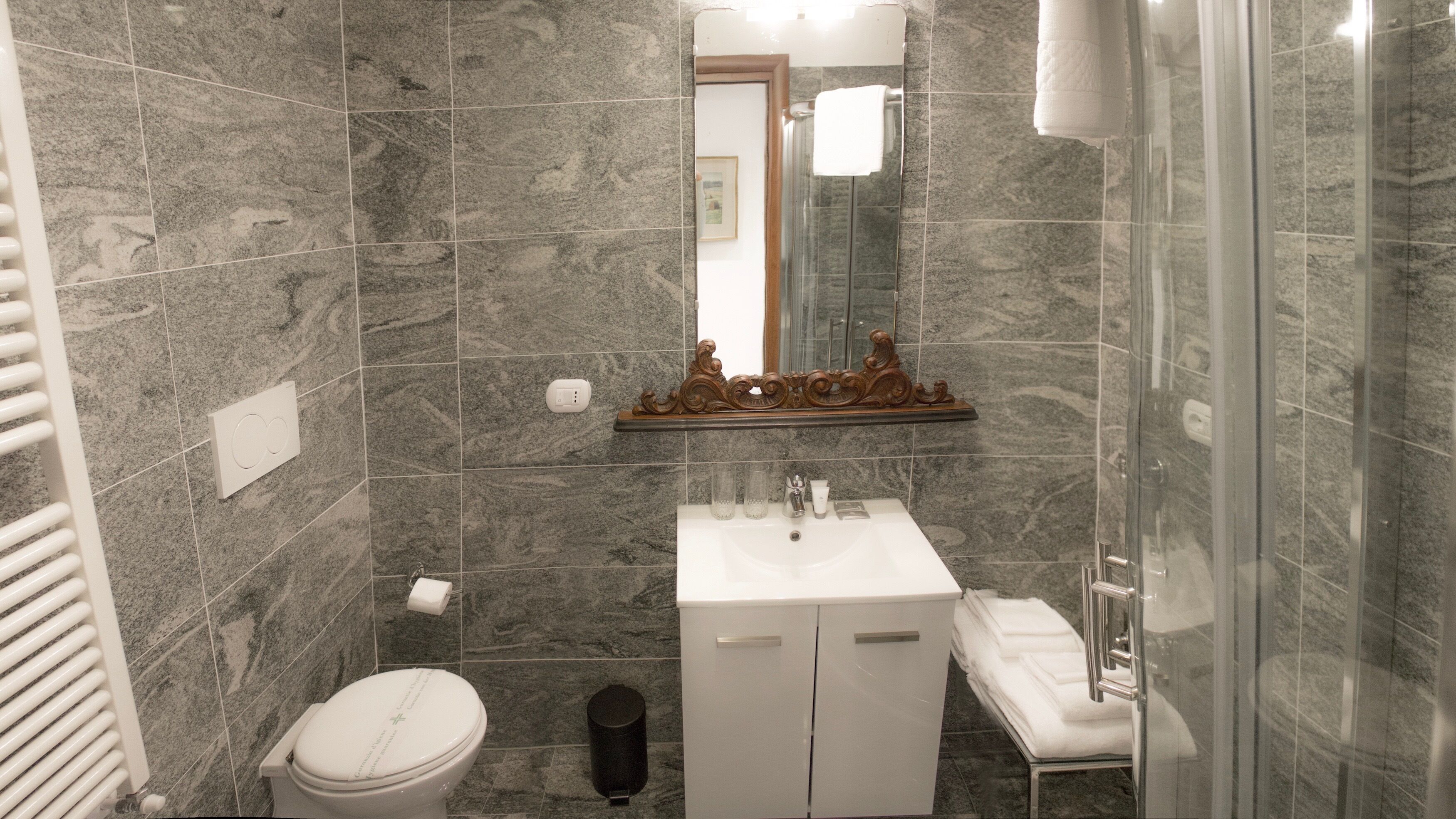 A bathroom with a marble wall, a white sink, a toilet, and a glass shower enclosure.