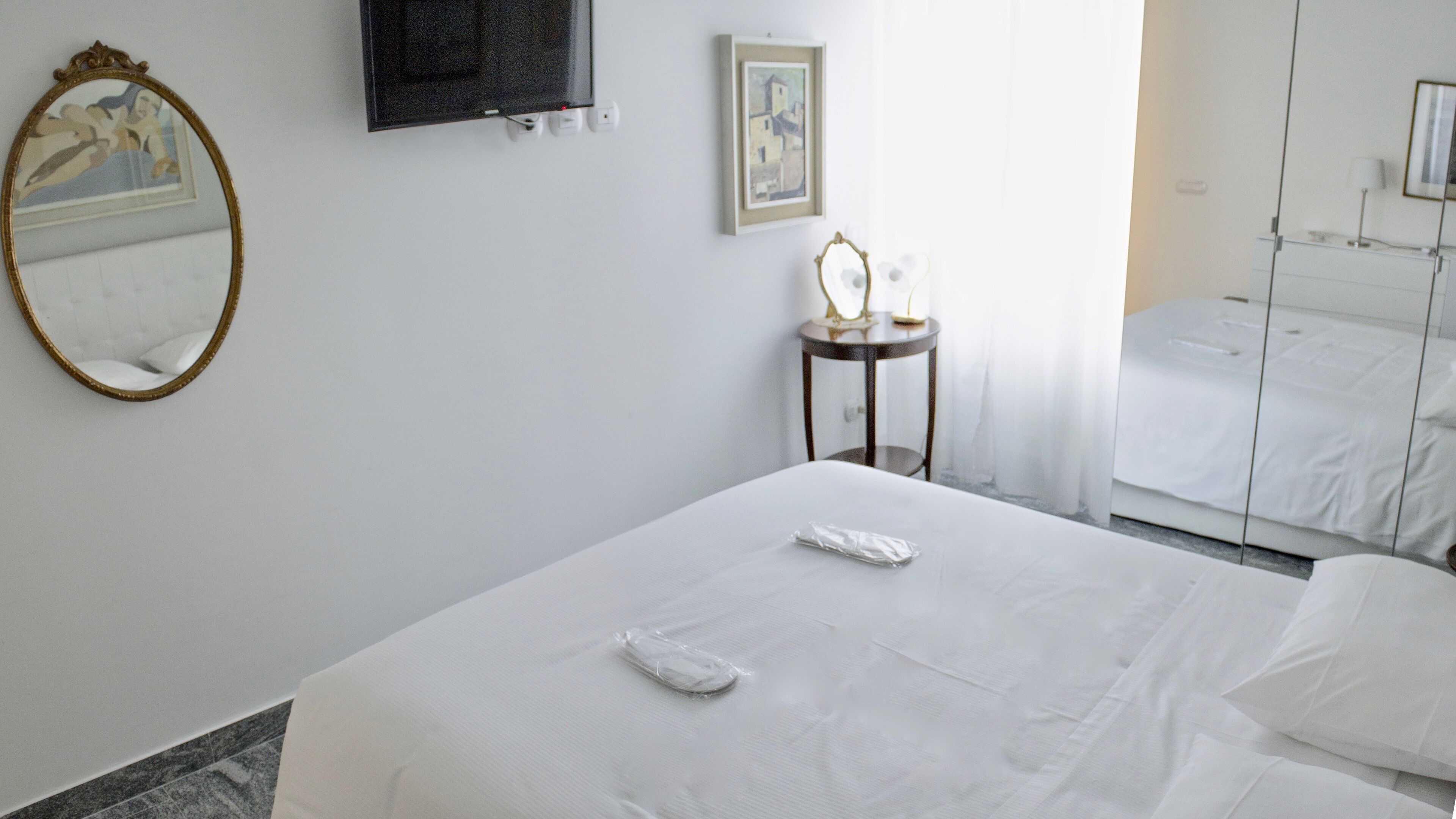 Ein Hotelzimmer mit Bett, Nachttisch mit Lampe, Spiegel und einem Gemälde an der Wand.