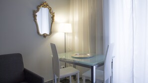 A hotel room with a glass dining table, two white chairs, a dark armchair, a mirror with an ornate frame, and a floor lamp. - Aiello Suites Executive (Milan)