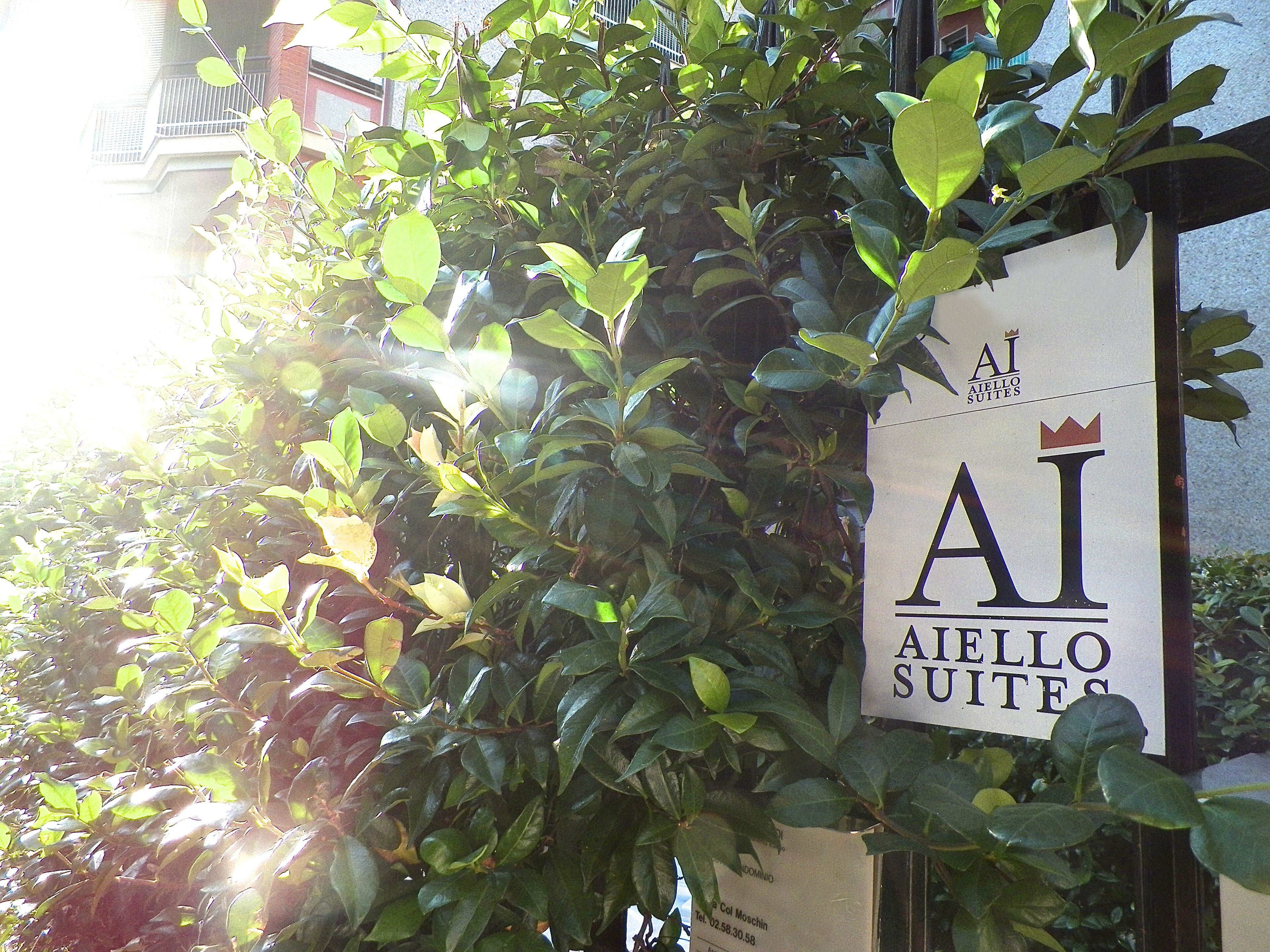 A sign for AIELLO SUITES with a partial view of a building in the background.