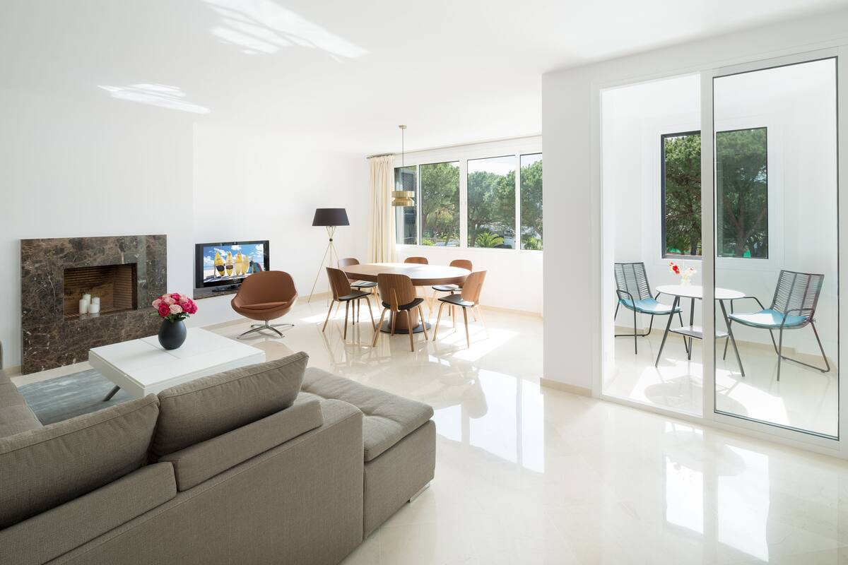 A modern living room with a sofa, a TV, a fireplace, and a dining area with chairs and a table.