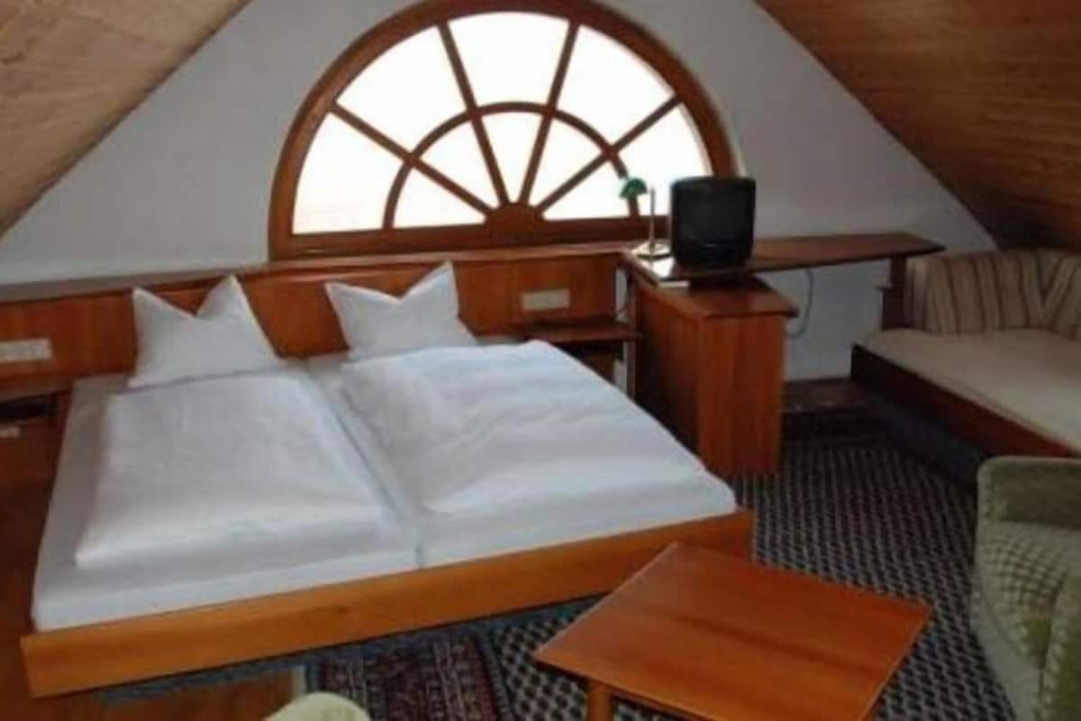 Acomodação aconchegante, em um único ambiente, com uma cama grande, uma mesa pequena, um sofá e uma televisão.