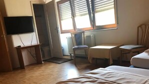 A hotel room with a bed, a desk, a chair, a television, and a window with blinds. - Gästehaus Denninger (Karlsbad)