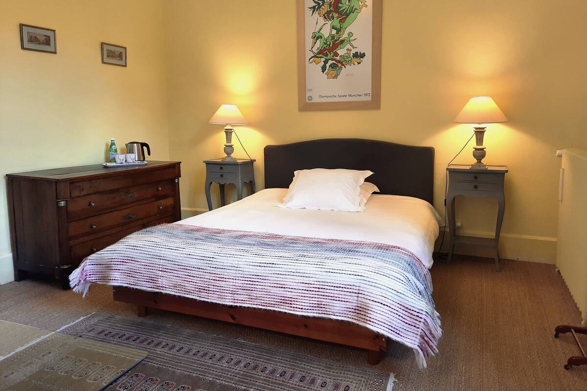 A bedroom with a bed, two bedside tables with lamps, a dresser, and a framed picture on the wall.