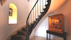 A curved staircase with a black railing, a small table with a display case, and a wall-mounted light fixture. - Les Tuileries du Buisson (Verneuil d'Avre et d'Iton)