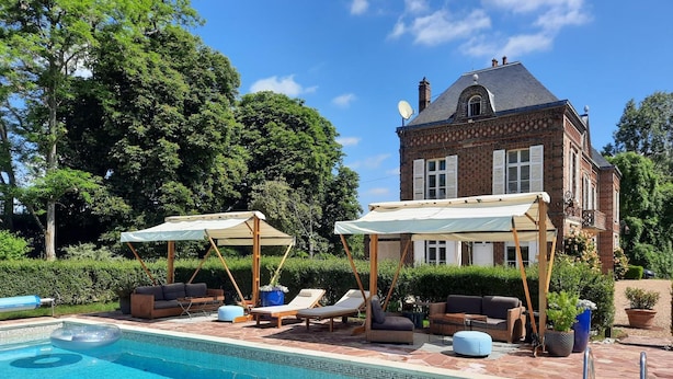 A pool area with lounge chairs and umbrellas, a brick house in the background, and a clear blue sky. - Les Tuileries du Buisson (Verneuil d'Avre et d'Iton)