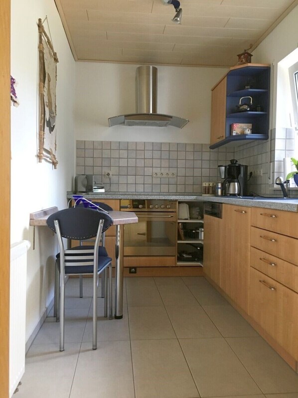 A compact kitchen with a gas stove, oven, and a small dining area with a chair. - Apartment cozy and modern (Edertal)