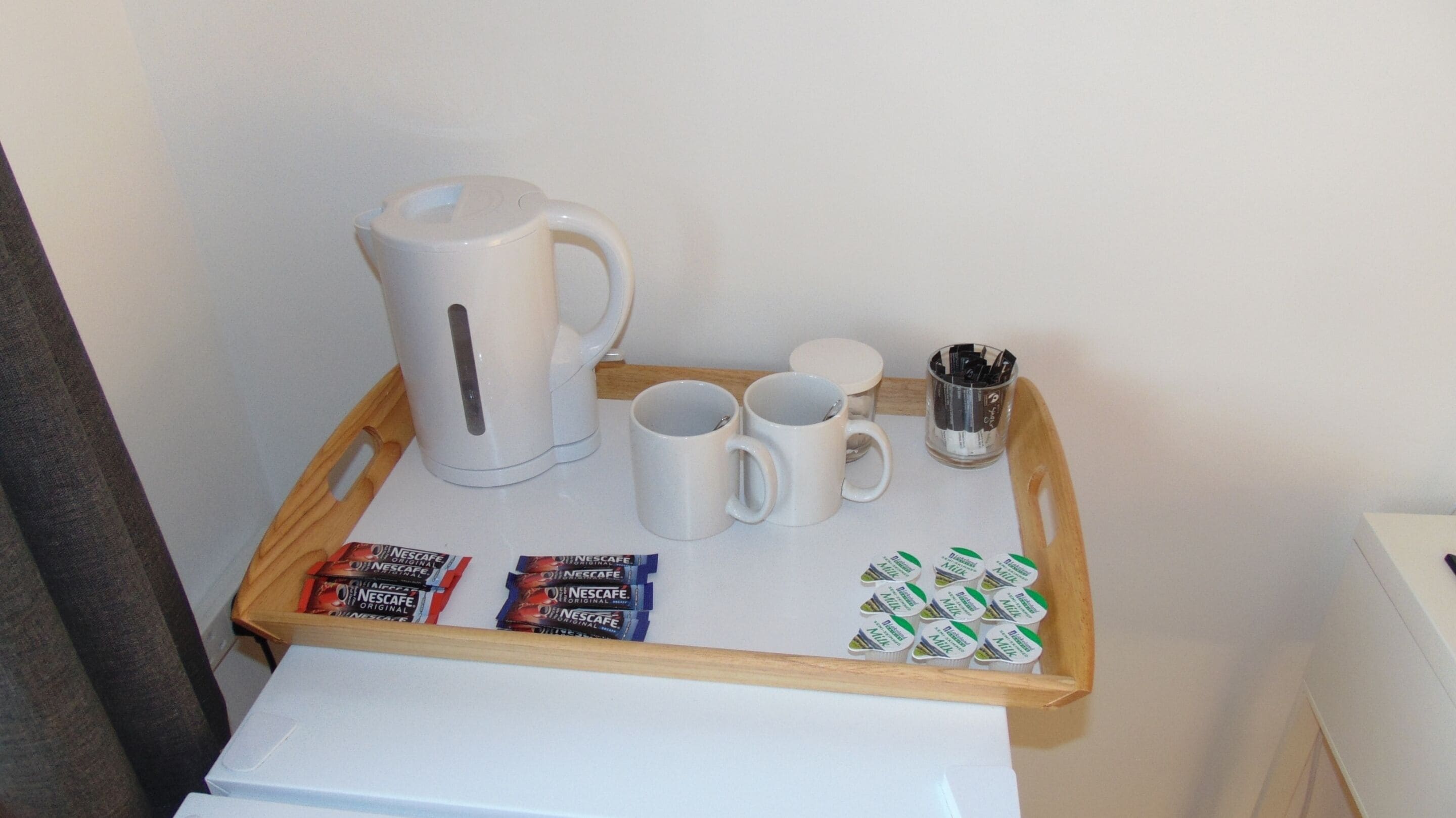 A tray with a coffee maker, two mugs, a glass of coffee, and packets of Nescafe Original instant coffee.