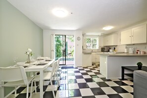 Una cucina moderna con mobili bianchi, un pavimento a scacchi bianchi e neri, e un'area pranzo con sedie bianche e un tavolo apparecchiato per due.