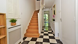A staircase with a checkered floor leading to a door, a potted plant on a console table, and a sign above the staircase. - Harlinger Lodge Annexe (London)
