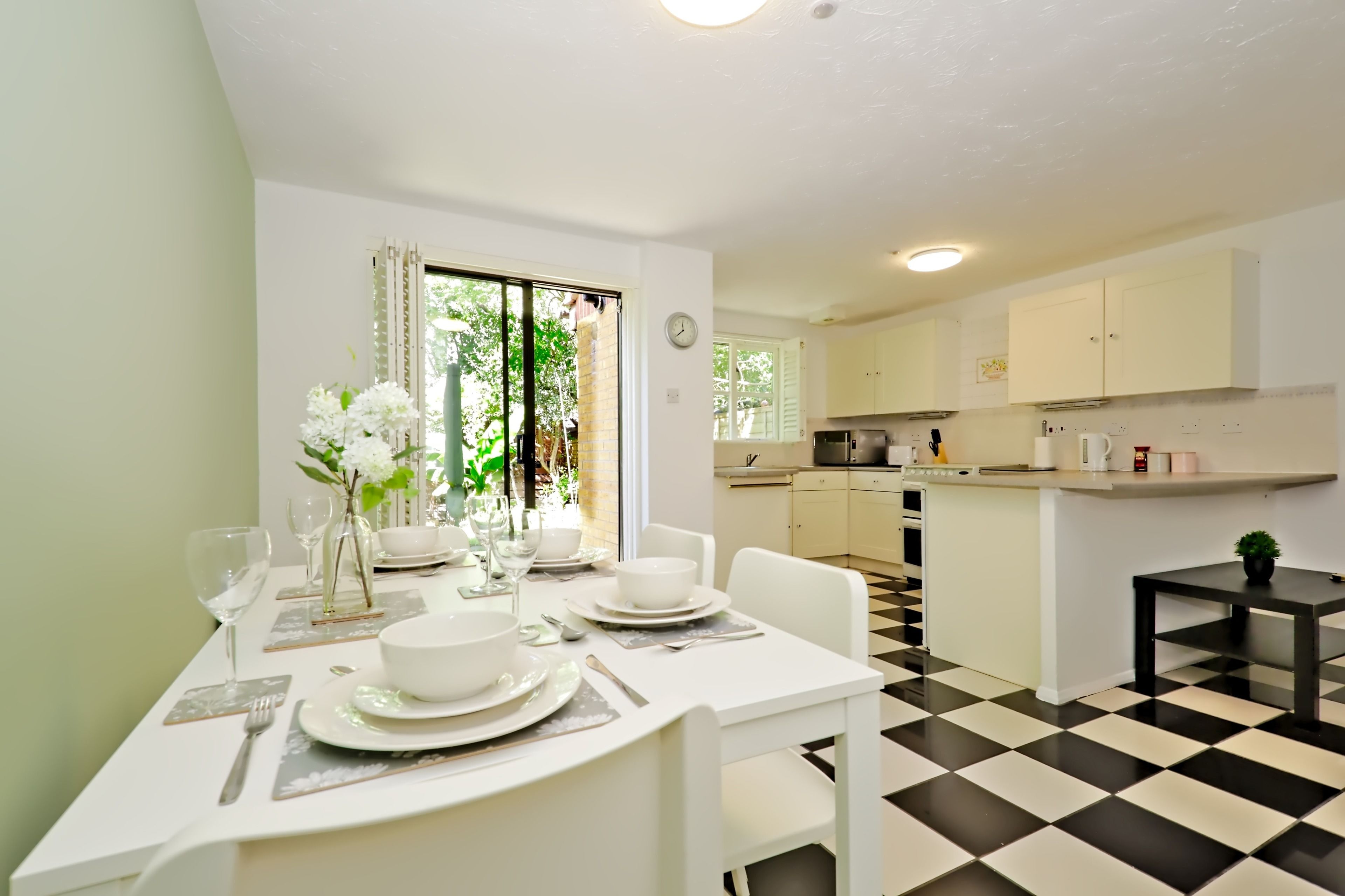 Un comedor con una mesa preparada para cuatro, una cocina al fondo y un suelo a cuadros.