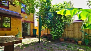 A patio with a wooden table, potted plants, and a brick wall. - Harlinger Lodge Annexe (London)