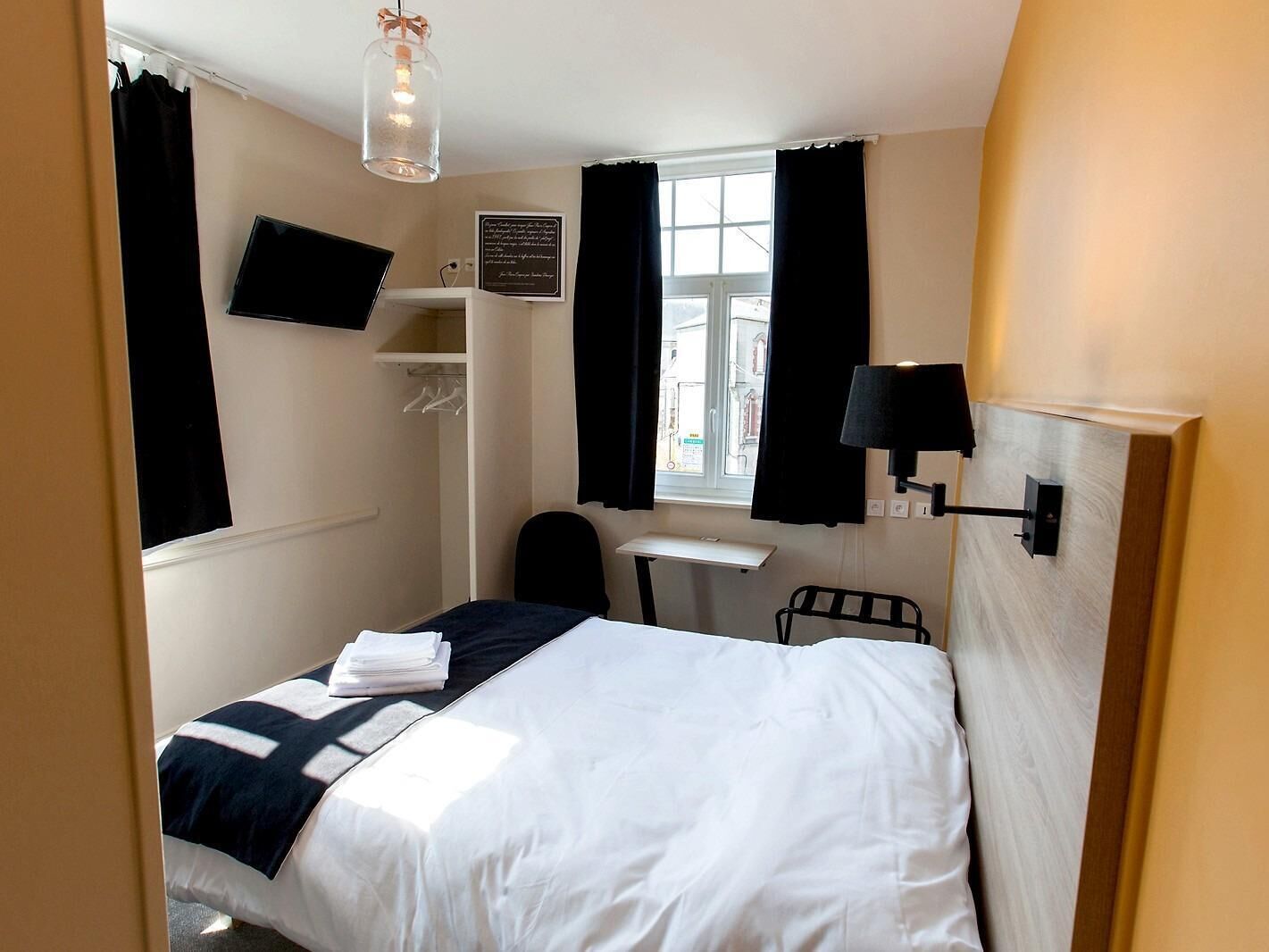 A hotel room with a bed, a desk, a chair, a TV, and a window with curtains.