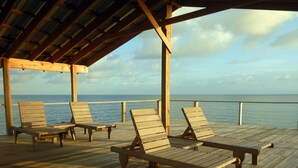 Eine Holzterrasse mit Liegestühlen mit Blick auf das Meer.