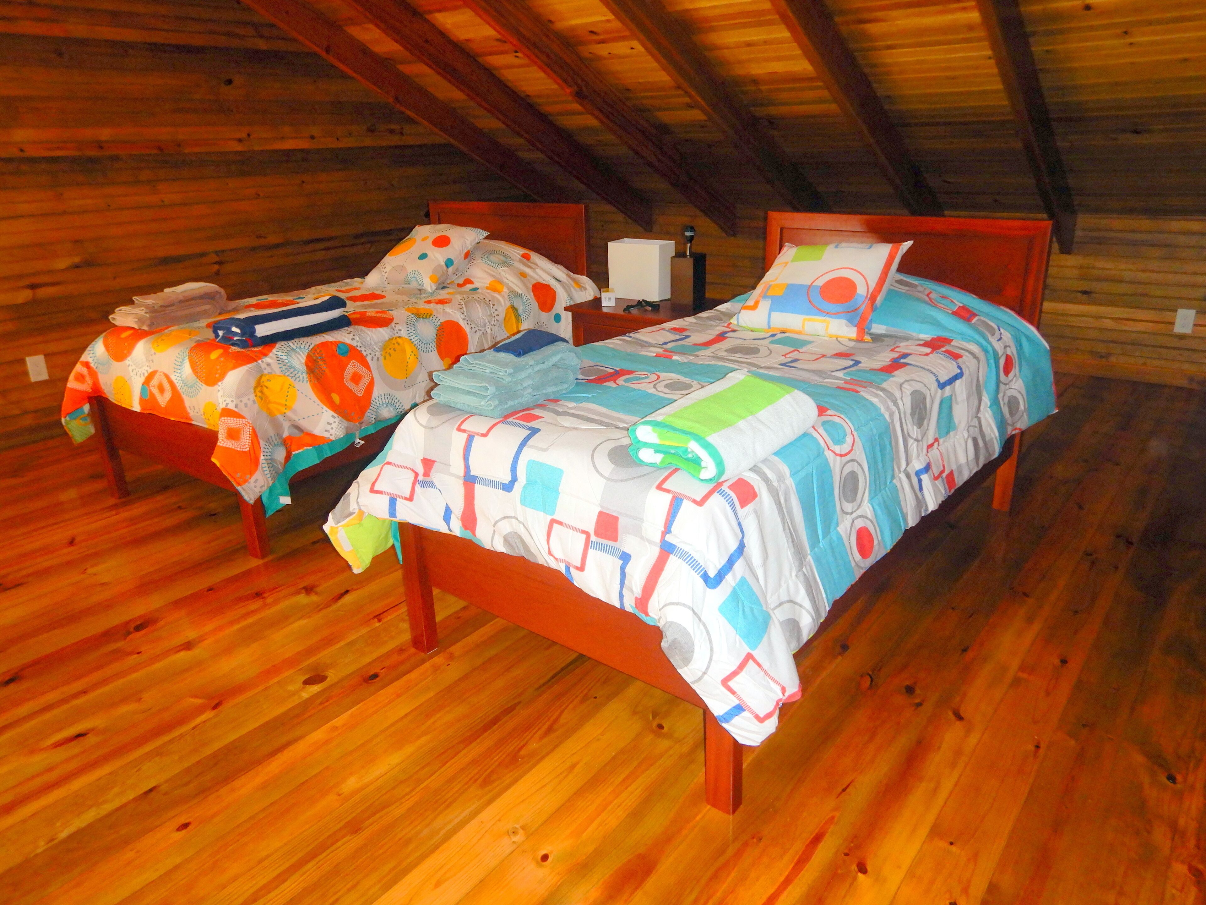 A cozy attic bedroom with two wooden beds, each with colorful bedding and a wooden headboard.