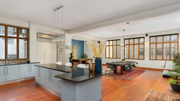 Eine geräumige Küche mit Kochinsel, Holzboden und großen Fenstern.