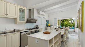 Una cocina moderna con armarios blancos, una isla central y un comedor con vistas al exterior.