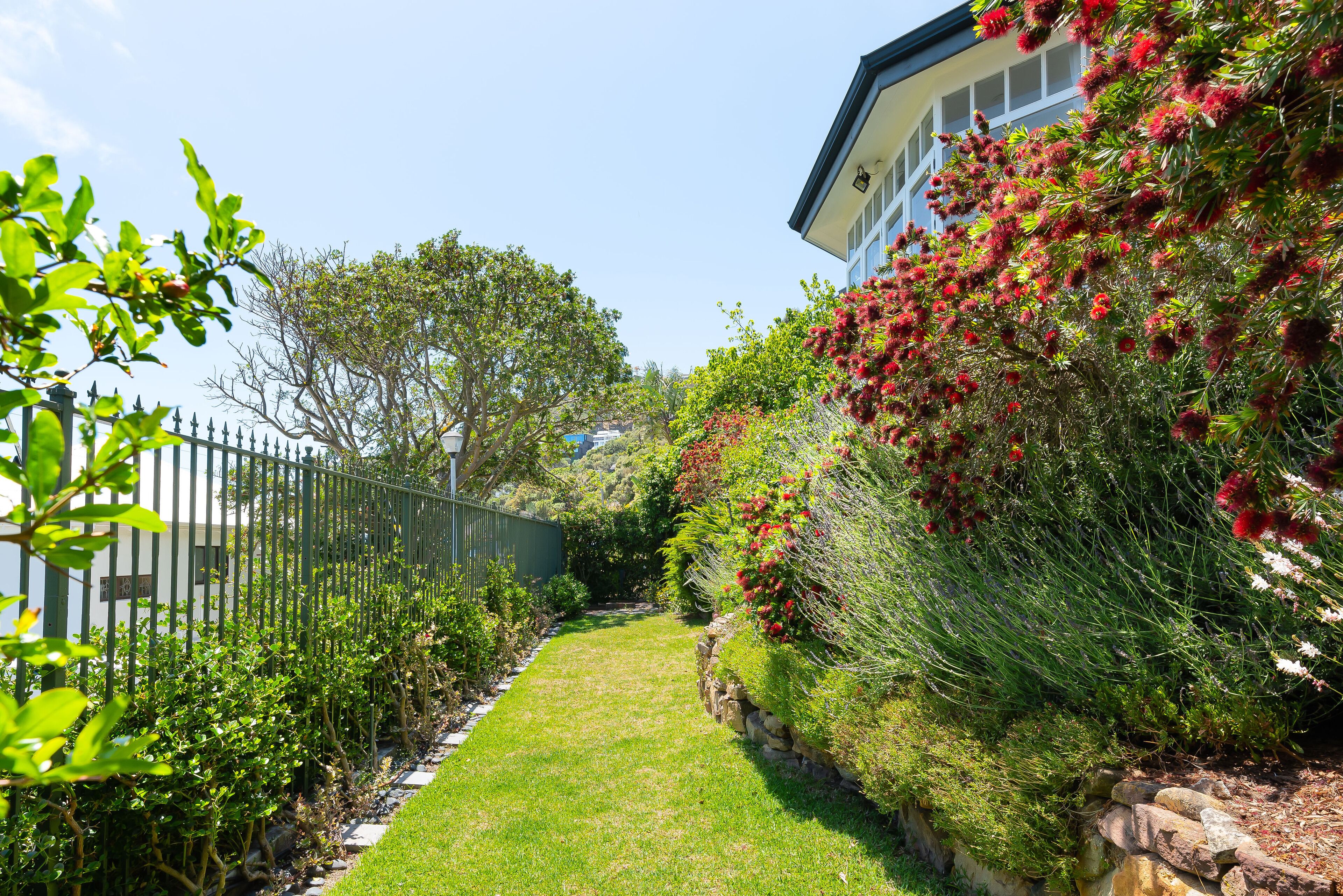 A well-maintained garden with a stone wall, a paved pathway, and a variety of plants and shrubs.